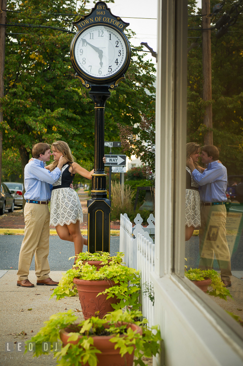 Engaged girl holding on clock and almost kissing fiancé. Oxford, Eastern Shore Maryland pre-wedding engagement photo session, by wedding photographers of Leo Dj Photography. http://leodjphoto.com