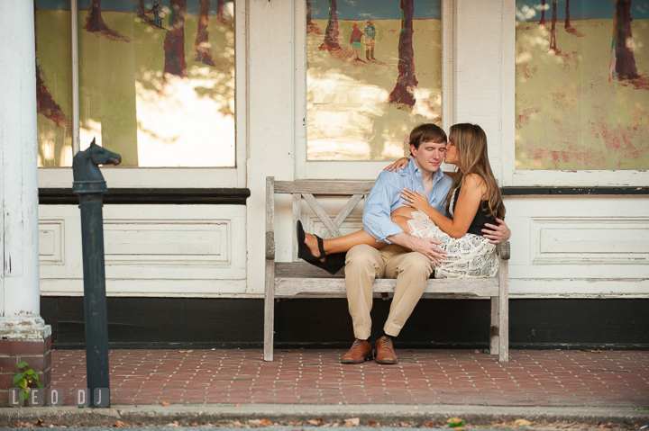 Engaged girl sitting on bench kissing fiancé's cheek. Oxford, Eastern Shore Maryland pre-wedding engagement photo session, by wedding photographers of Leo Dj Photography. http://leodjphoto.com