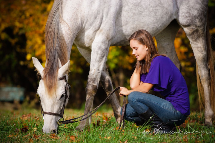 Horse eating grass while girl owner squatting beside it. Annapolis Kent Island Maryland High School Senior Portrait Photography with Horse Pet by photographer Leo Dj