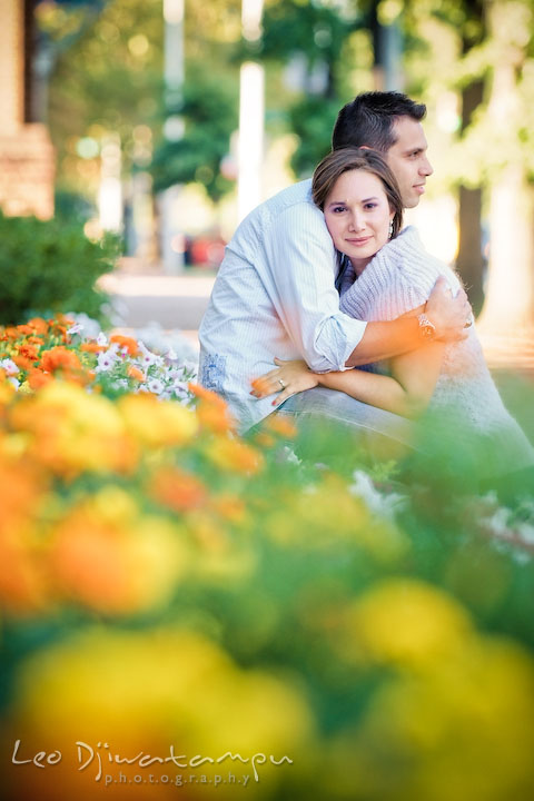 Engaged girl hugged by her fiancee by the flower bed. Candid Old Town Alexandria Virginia Engagement Photography Session by Wedding Photographer Leo Dj