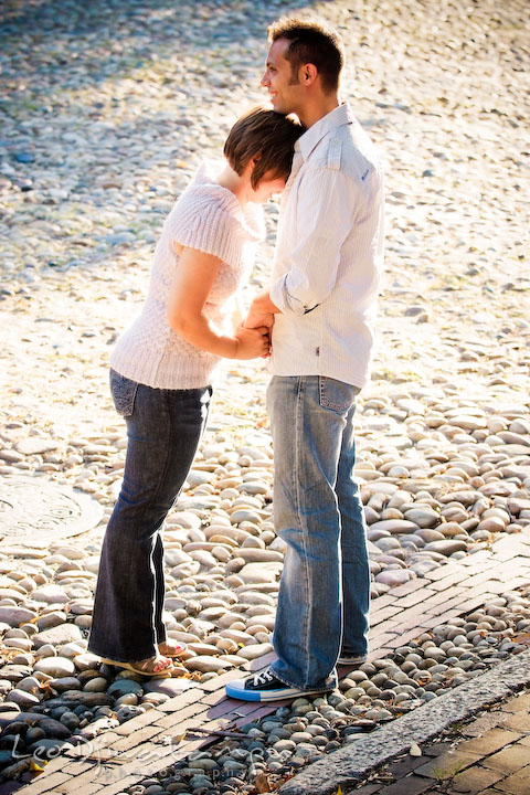 Engaged couple holding hands, laughing, on a cobble stone street. Candid Old Town Alexandria Virginia Engagement Photography Session by Wedding Photographer Leo Dj