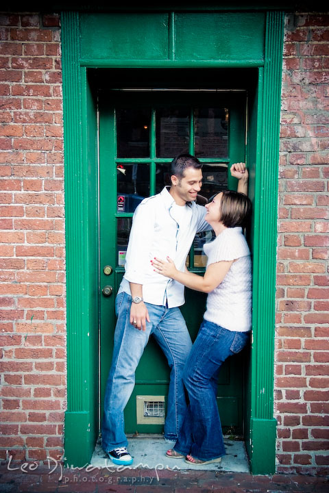 Engaged couple talking by a green door and frame. Candid Old Town Alexandria Virginia Engagement Photography Session by Wedding Photographer Leo Dj