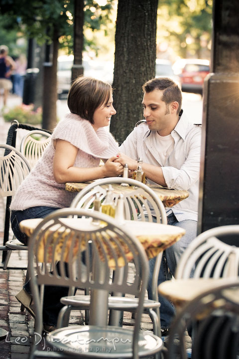 Engaged couple holding hand at an outdoor restaurant table. Candid Old Town Alexandria Virginia Engagement Photography Session by Wedding Photographer Leo Dj