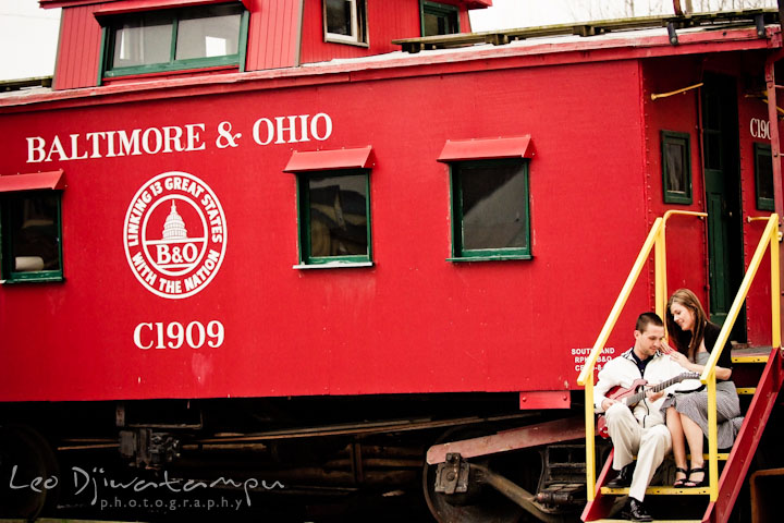 Engaged guy and girl sitting by a red caboose. Pre-Wedding Engagement Photo Session at Sykesville Maryland with Train Rail and Caboose by wedding photographer Leo Dj Photography