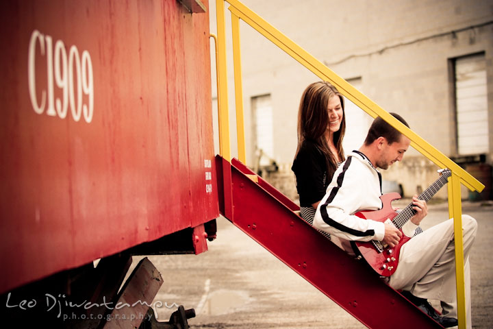 Engaged guy playing his red electric guitar and his fiancée laughing. Pre-Wedding Engagement Photo Session at Sykesville Maryland with Train Rail and Caboose by wedding photographer Leo Dj Photography