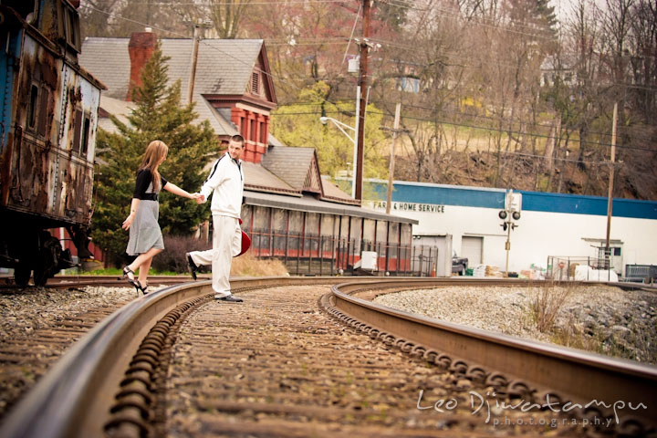 Engaged guy leading his fiancée through train tracks. Pre-Wedding Engagement Photo Session at Sykesville Maryland with Train Rail and Caboose by wedding photographer Leo Dj Photography