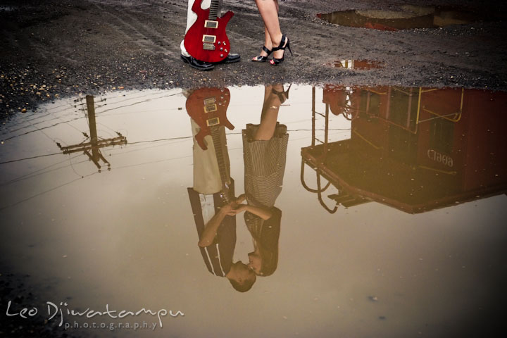 Engaged girl cuddling with her fiancé. Image of them and red caboose reflected on a puddle. Pre-Wedding Engagement Photo Session at Sykesville Maryland with Train Rail and Caboose by wedding photographer Leo Dj Photography