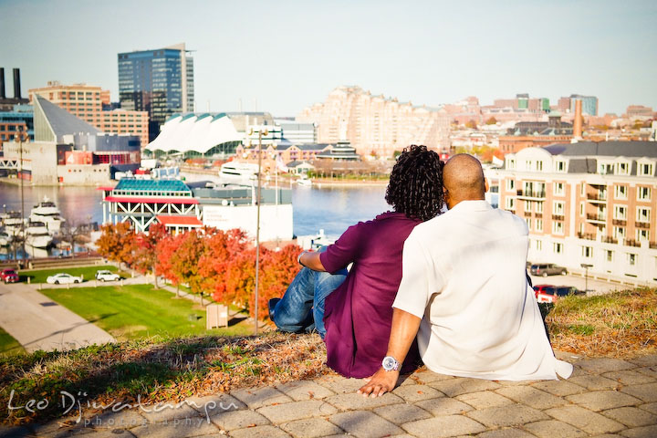 engaged couple sitting by the edge, overlooking the Baltimore City inner harbor. Federal Hill Park Baltimore pre-wedding engagement portrait