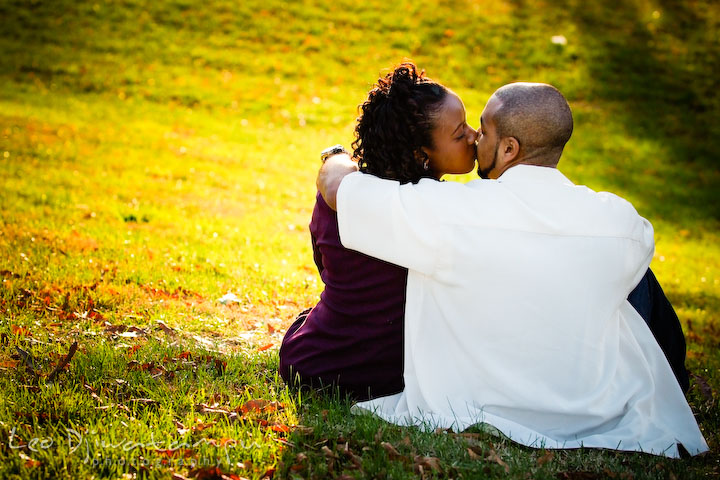 engaged couple sitting on green grass, kissing. Federal Hill Park Baltimore pre-wedding engagement portrait