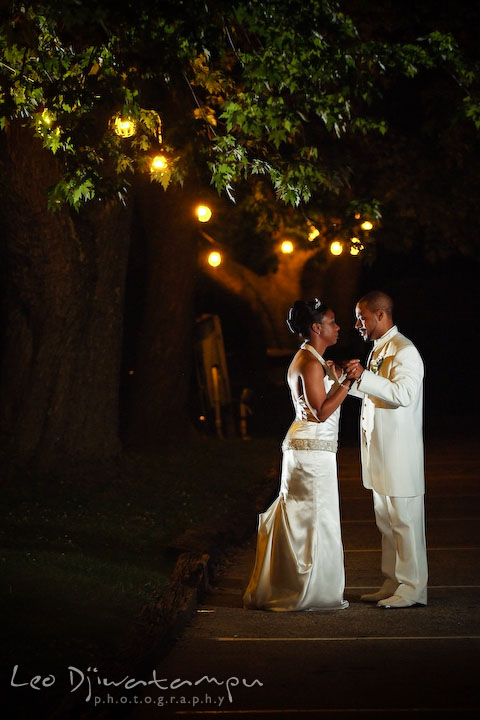 Bride and groom holding hands outdoor in the evening, with yellow string of lights on the trees. Wedding photography at Padonia Park Club at Towson, Timonium-Cockeysville area, North of Baltimore