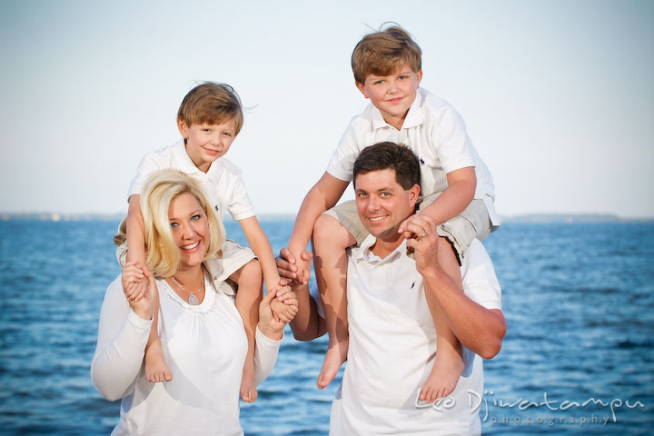 Children carried on mom and dad's shoulder at the beach with blue sea water. Kent Island, Annapolis, MD Fun Candid Family Lifestyle Photographer, Leo Dj Photography