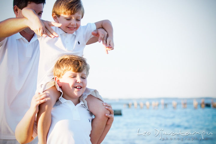 A boy carrying his brother on his shoulder with a help from their father. Kent Island, Annapolis, MD Fun Candid Family Lifestyle Photographer, Leo Dj Photography