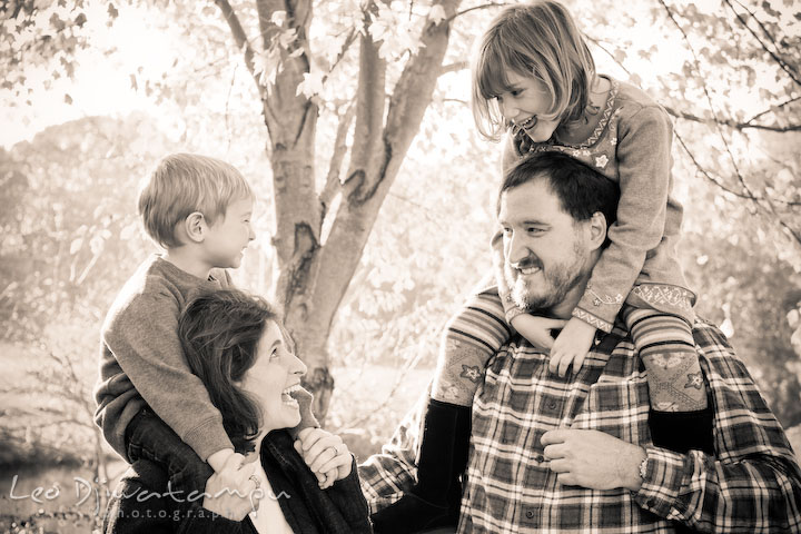 brother and sister on parent's shoulder, looking at each other, laughing. Fun candid family children lifestyle photographer Annapolis Maryland