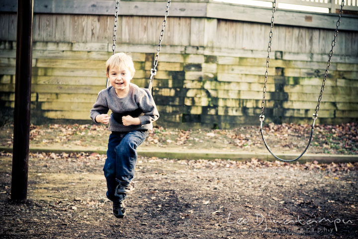 boy playing swing on park playground, smiling. Fun candid family children lifestyle photographer Annapolis Maryland