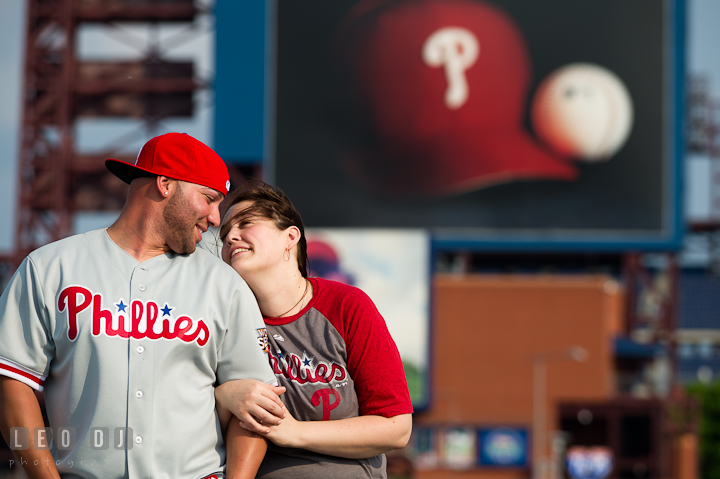 Engaged couple wearing Phillies jersey, hat, and t-shirt. Pre-wedding or engagement photo session at Phillies Ball Park, Love Park, Philadelphia, by wedding photographers of Leo Dj Photography.