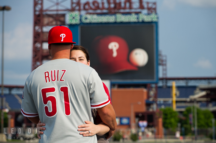 Engaged guy wearing Phillies Ruiz 51 jersey hugged his fiancée. Pre-wedding or engagement photo session at Phillies Ball Park, Love Park, Philadelphia, by wedding photographers of Leo Dj Photography.