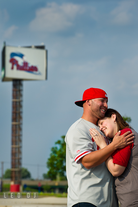 Engaged girl cuddled with her fiancé. Pre-wedding or engagement photo session at Phillies Ball Park, Love Park, Philadelphia, by wedding photographers of Leo Dj Photography.