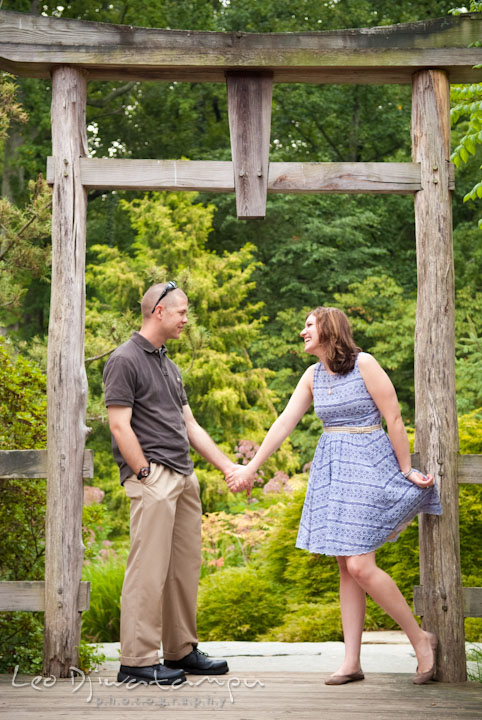 Engaged guy holding his fiancée under a Japanese gazebo arch. Pre-wedding engagement photo session at Brookside Gardens, Wheaton, Silver Spring, Maryland, by wedding photographer Leo Dj Photography.