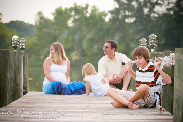 Boy or son posing on pier with his lacrosse stick, family in the back. Kent Island and Annapolis, Eastern Shore, Maryland Candid Family Maternity Session Photographer