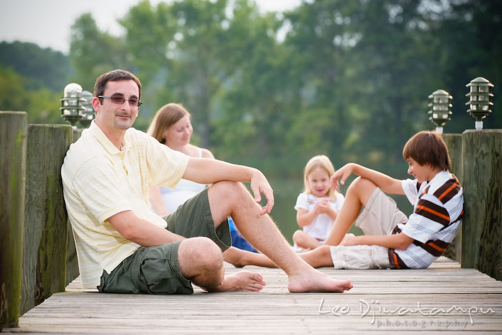 The father posing on pier, the rest of the family in the background. Kent Island and Annapolis, Eastern Shore, Maryland Candid Family Maternity Session Photographer