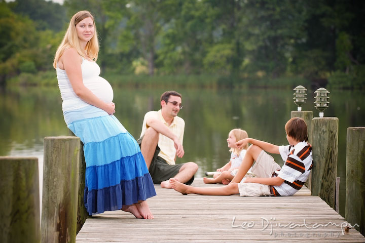 Pregnant mother posing on pier with family in the background talking to each other. Kent Island and Annapolis, Eastern Shore, Maryland Candid Family Maternity Session Photographer