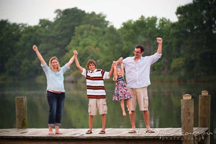 Family (mother, son, daughter, and father) standing on pier raising hands up in the air. Kent Island and Annapolis, Eastern Shore, Maryland Candid Family Maternity Session Photographer