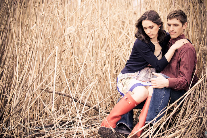 couple with red boots, sitting by tall grasses, looking down. Engagement session model photography - Annapolis photographer
