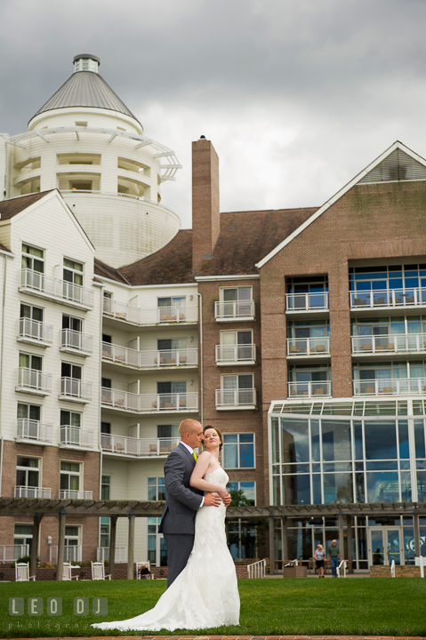 Groom hugging Bride from behind with the hotel and Ravens' View in the background. Hyatt Regency Chesapeake Bay wedding at Cambridge Maryland, by wedding photographers of Leo Dj Photography. http://leodjphoto.com