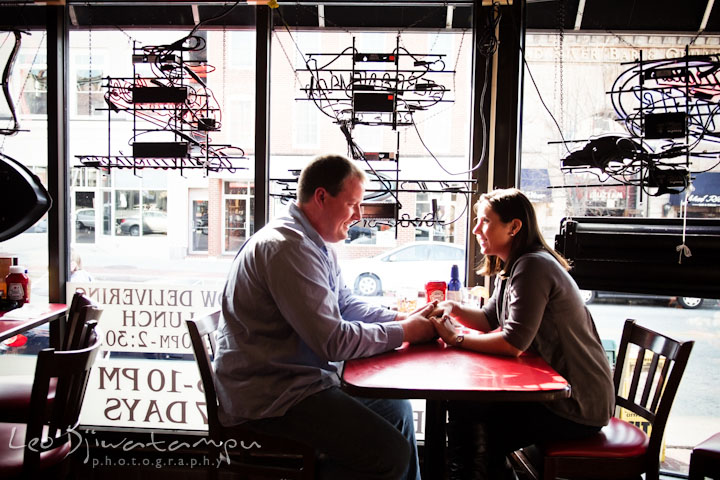 A guy and his fiancée sitting and holding hands. Pre-wedding Engagement Photo Session Federal Hill Baltimore and Mother's Grille restaurant bar by wedding photographer Leo Dj Photography