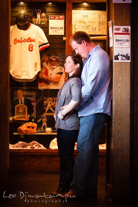 Engaged guy hugging his fiancée by the Orioles jersey display. Pre-wedding Engagement Photo Session Federal Hill Baltimore and Mother's Grille restaurant bar by wedding photographer Leo Dj Photography