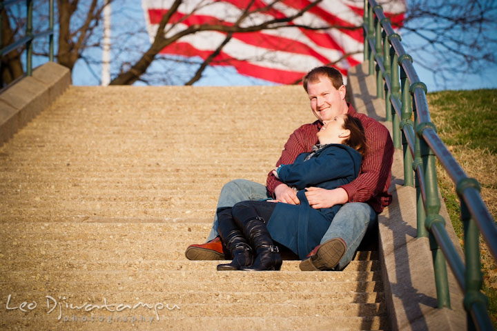 Engaged girl sitting and leaning on fiancé, laughing. American flag in the background. Pre-wedding Engagement Photo Session Federal Hill Baltimore and Mother's Grille restaurant bar by wedding photographer Leo Dj Photography