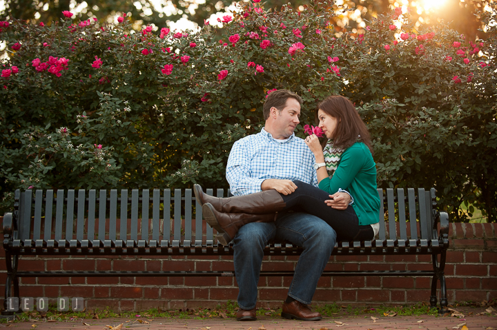 Engaged girl sitting on a bench with her fiancé smelling red rose. Annapolis Eastern Shore Maryland pre-wedding engagement photo session at downtown, by wedding photographers of Leo Dj Photography. http://leodjphoto.com