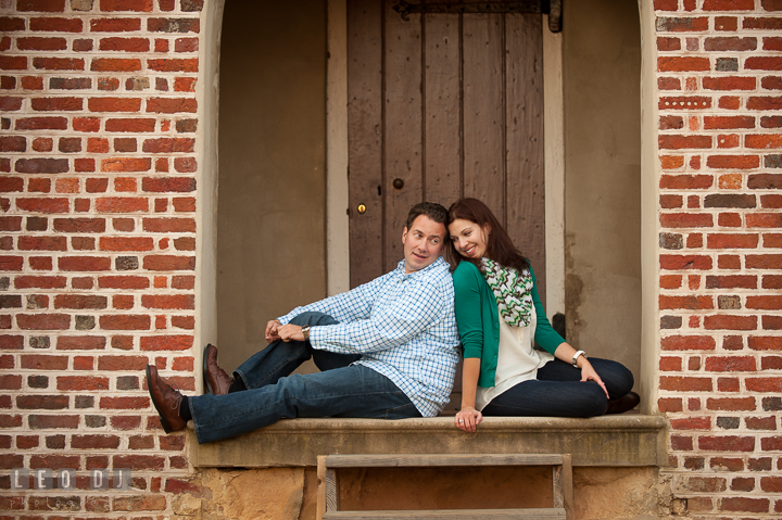 Engaged couple leaning their backs against each other under a brick building arch. Annapolis Eastern Shore Maryland pre-wedding engagement photo session at downtown, by wedding photographers of Leo Dj Photography. http://leodjphoto.com