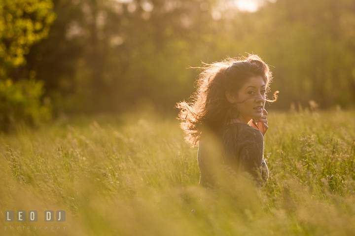 Girl in grass meadow looking back while wind blowing her hair. Eastern Shore, Maryland, Kent Island High School senior portrait session by photographer Leo Dj Photography. http://leodjphoto.com