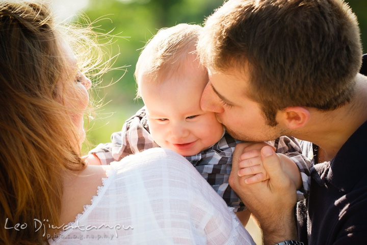 Mother holding baby over her shoulder. Father holds baby's hand and kissed him. Eastern Shore Maryland Kent Island Family Lifestyle Portrait Photo Session by Photographer Leo Dj Photography