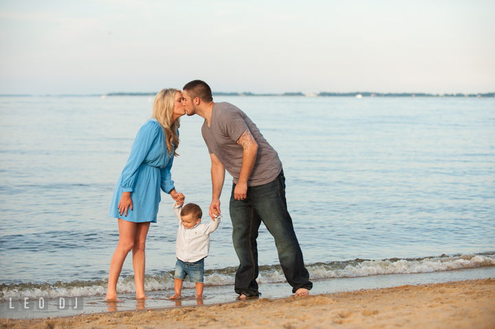 Mom and Dad kissing while holding their child in the middle. Kent Island, Annapolis, Eastern Shore Maryland candid children and family lifestyle portrait photo session by photographers of Leo Dj Photography. http://leodjphoto.com