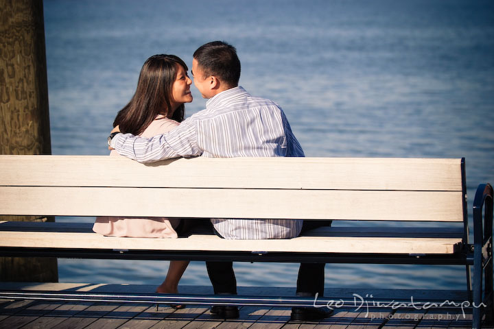 Engaged couple sitting on a bench by a water, touching their noses. National Harbor, Gaylord National Hotel pre-wedding engagement photo session