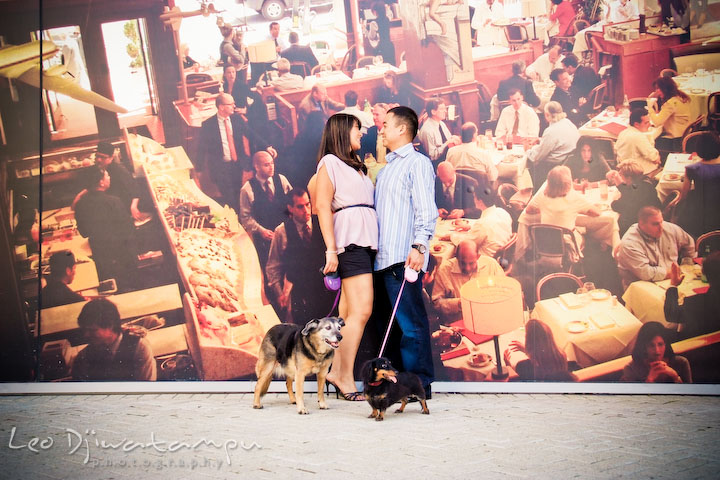 Fiancée, fiancé, and their dogs standing by a large photo wall. National Harbor, Gaylord National Hotel pre-wedding engagement photo session