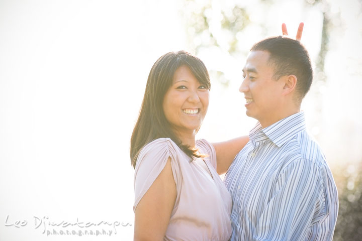 An engaged girl giving the rabbit ear gesture behind her fiancé's head. National Harbor, Gaylord National Hotel pre-wedding engagement photo session