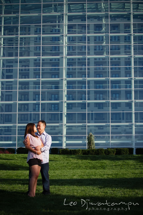 Engaged couple holding each other with the large structure in the back. National Harbor, Gaylord National Hotel pre-wedding engagement photo session