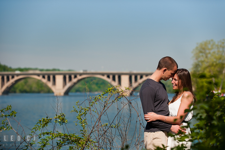 Engaged couple hugging by DC Waterfront with the Francis Scott Key Bridge in the background. Georgetown Washington DC pre-wedding engagement photo session, by wedding photographers of Leo Dj Photography. http://leodjphoto.com