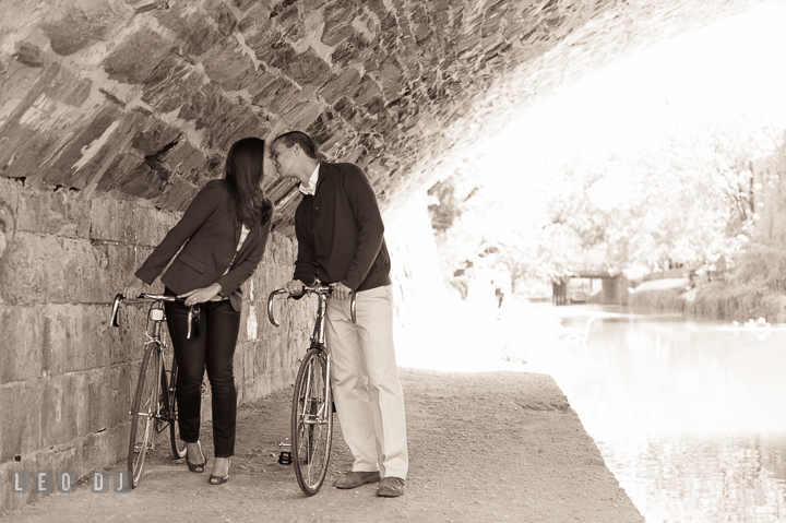 Engaged couple holding bicycles and kissed under a stone bridge over the C&O canal. Georgetown Washington DC pre-wedding engagement photo session, by wedding photographers of Leo Dj Photography. http://leodjphoto.com