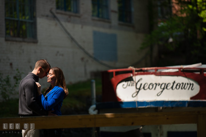 Engaged guy hugging with his fiancée at the C&O Canal with The Georgetown boat in the background. Georgetown Washington DC pre-wedding engagement photo session, by wedding photographers of Leo Dj Photography. http://leodjphoto.com