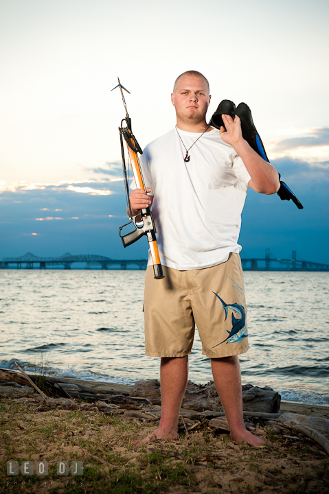 Guy holding flippers and speargun with the Chesapeake Bay Bridge in the background. Eastern Shore, Maryland, Kent Island High School senior portrait session by photographer Leo Dj Photography. http://leodjphoto.com